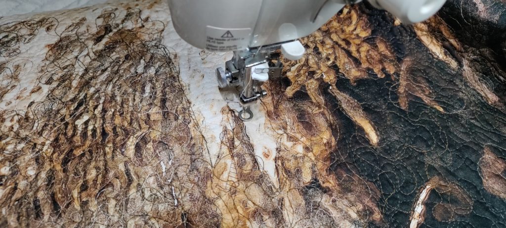 Nature's Window Buffalo panel in a sewing machine being free-motion quilted in circular stitching in brown and tan threads to create the texture of buffalo fur