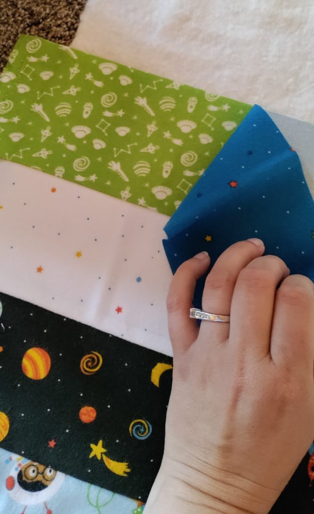 A hand carefully placing a strip of fabric on top of another strip of fabric so the edges line up