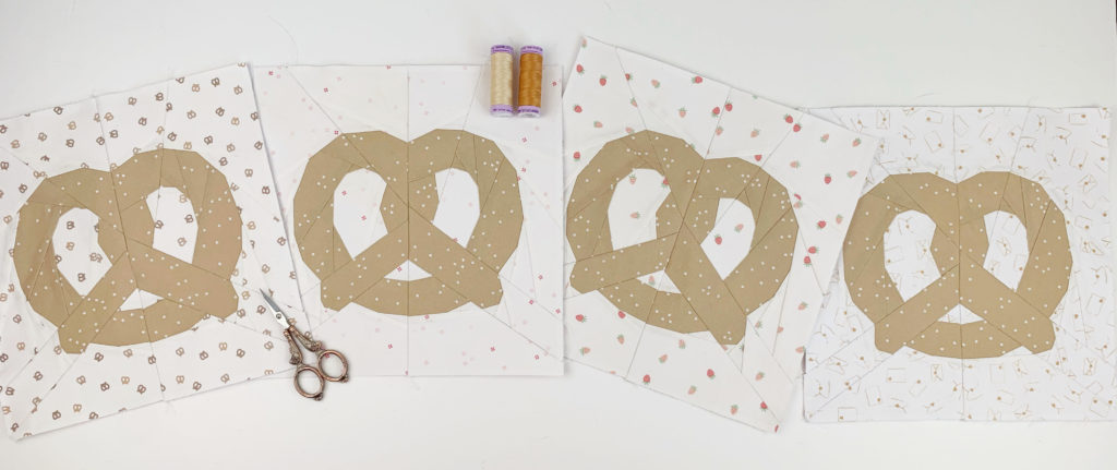 4 pretzel quilt blocks using creme and white fabric as background , the pretzels are light brown