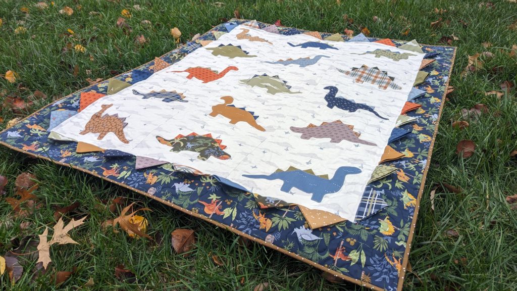 Applique dinosaur quilt with prairie point spikes and border details using the fabric collection Cretaceous