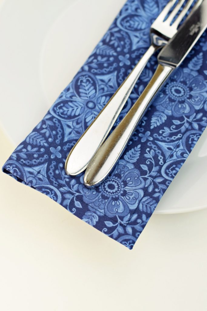 a quilted cotton napkin in blue print on a plate with a fork and a knife placed over it