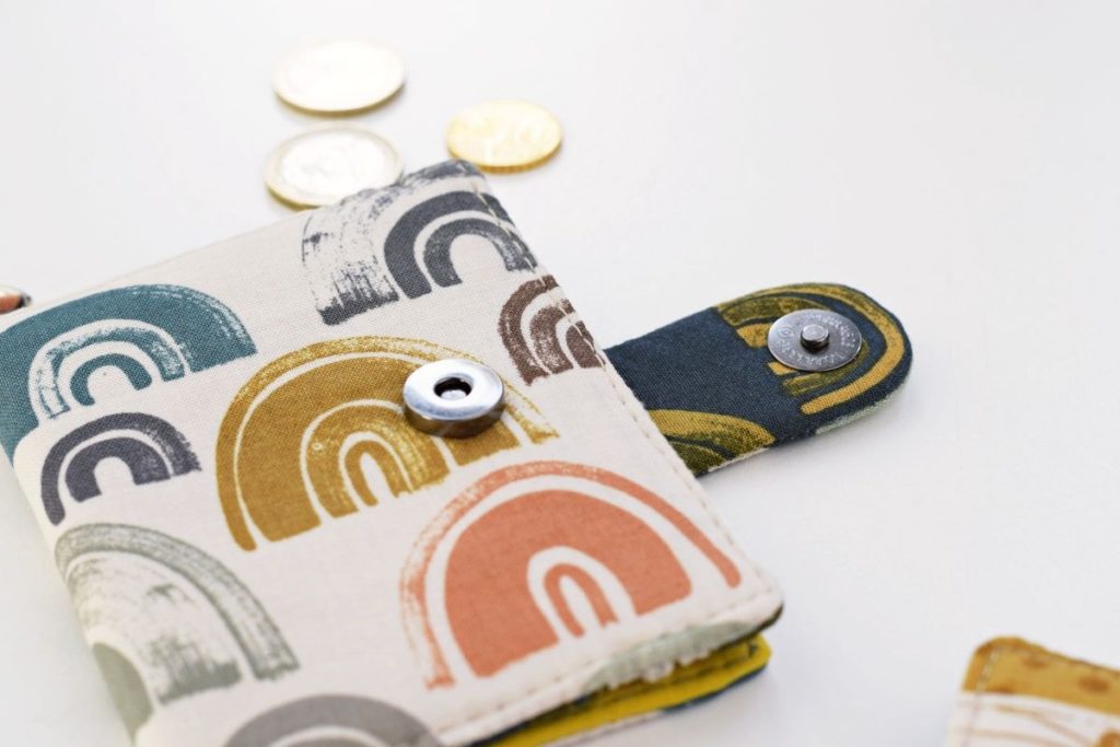 small bifold wallet with magnetic snap closure on a flat surface, with three coins in the background