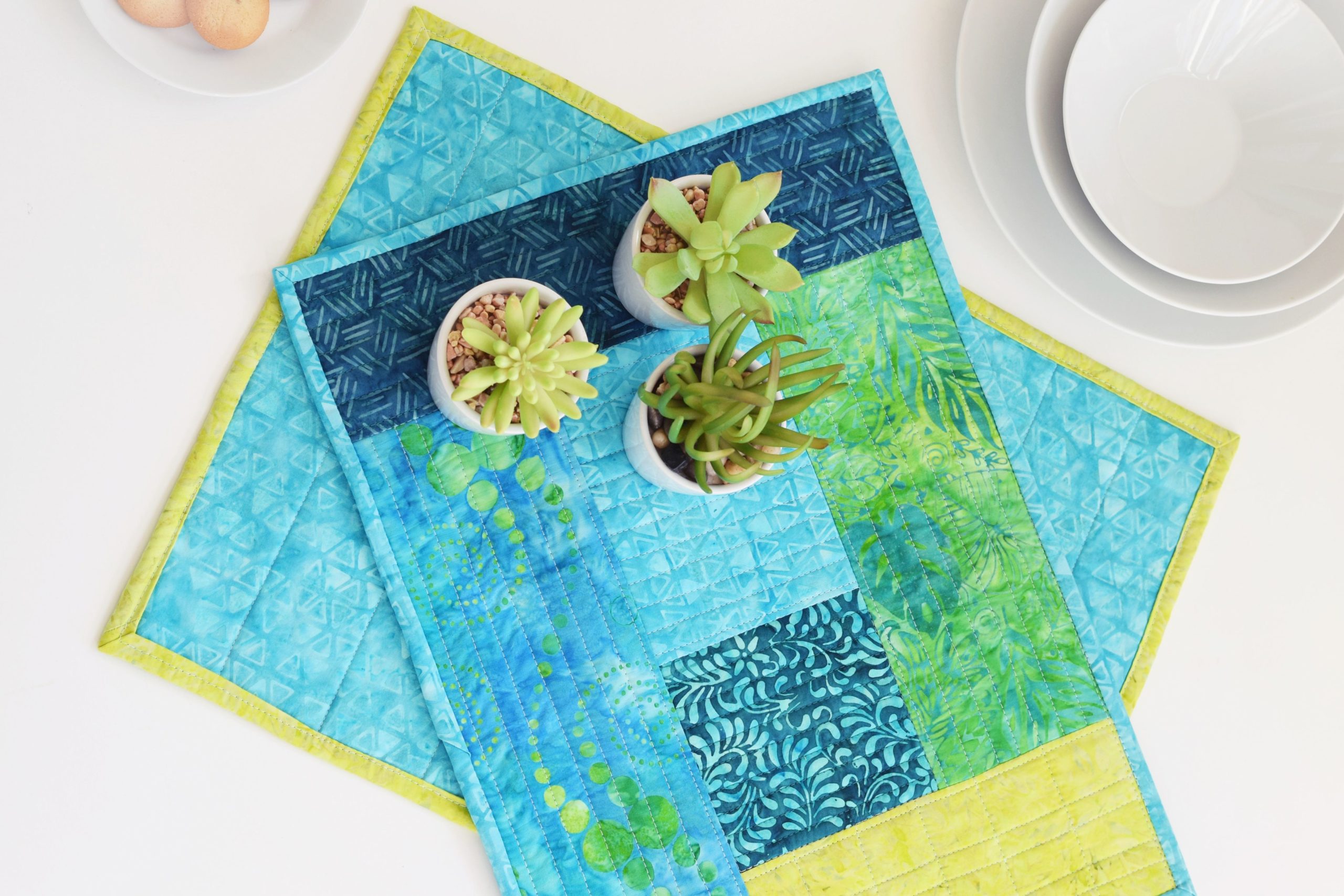 aqua and green color quilted placemat with little flower pots with succulents on the placemat
