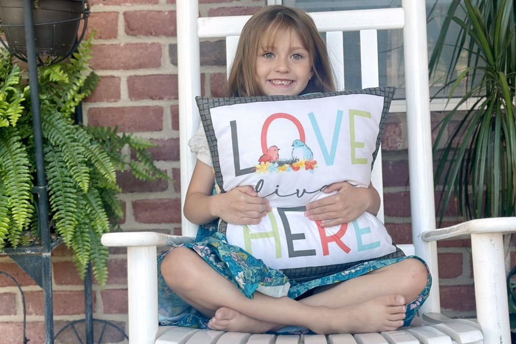 little girl holding a pillow that says "Love lives here" - Happy at Home fabric by Tara Reed