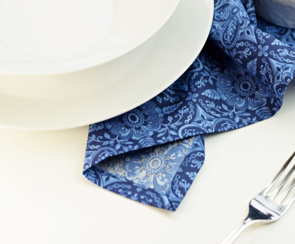 blue napkin showing a mitered corner next to a fork